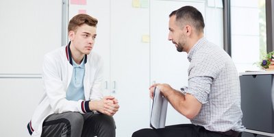 ein Mann sitzt mit einem Jugendlichen in seinem Büro bei einem Gespräch