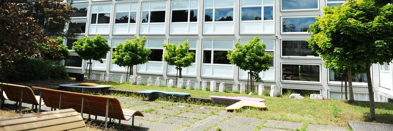 Schulhof mit Bänken und Bäumen vor dem Schulgebäude des Rotenbühl Gymnasium Saarbrücken