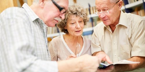 Drei Senioren schauen gemeinsam in ein Buch und beratschlagen sich